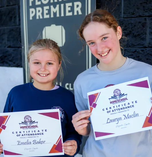 Two smiling young girls proudly displaying their soccer certificates of attendance at Braden River Soccer Club.